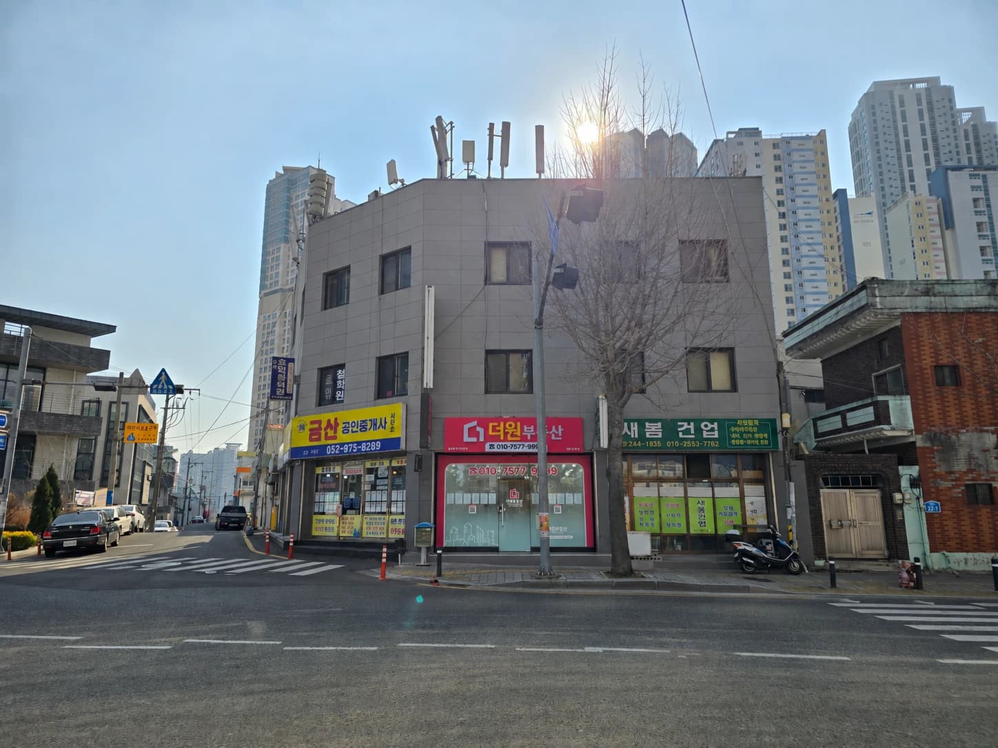 길 건너에서 본 더원부동산 사무소 전경. 건물 1층 가운데 꽃분홍색 간판이 있습니다.